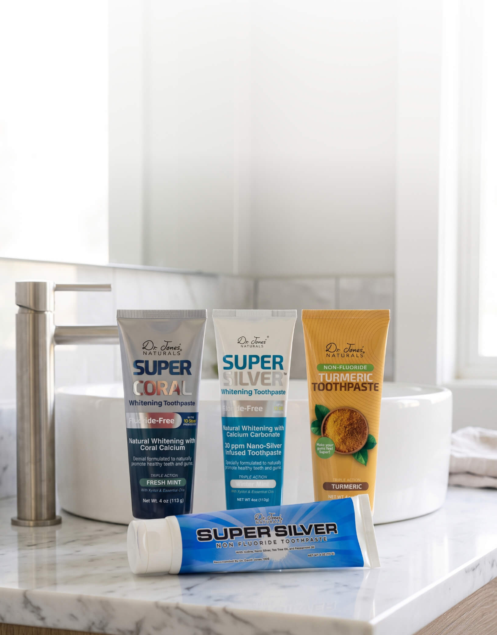 Dr. Jones' Naturals Super Coral, Super Silver and Turmeric toothpaste tubes on a marble bathroom counter